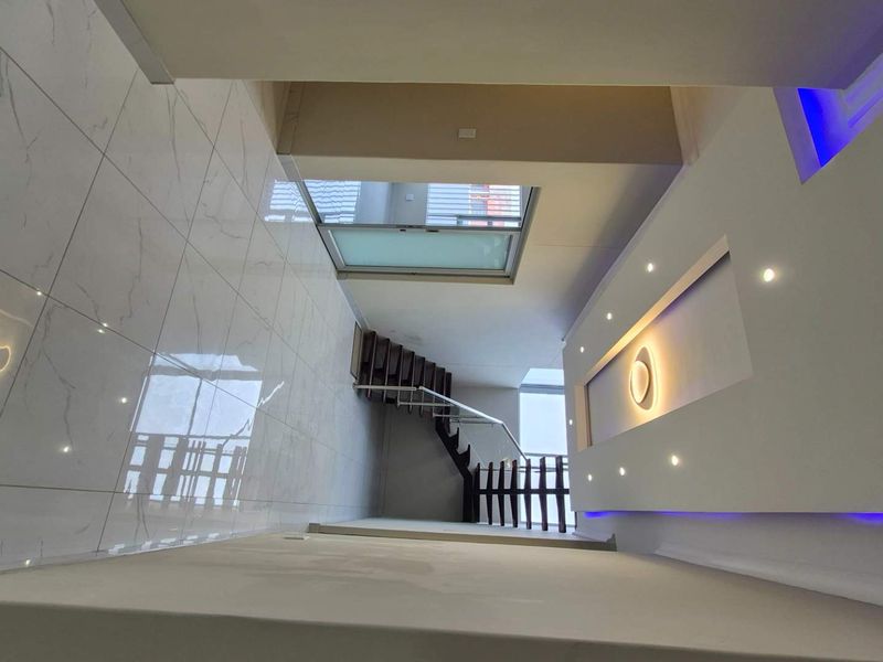 Modern double-volume entrance hall featuring polished porcelain floor tiles, a contemporary staircase with metal balustrade, and sophisticated recessed and cove ceiling lighting.