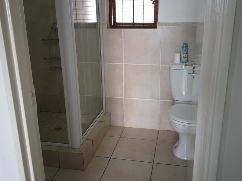 A functional bathroom featuring a shower enclosure, toilet, and neutral tiled finishes throughout.