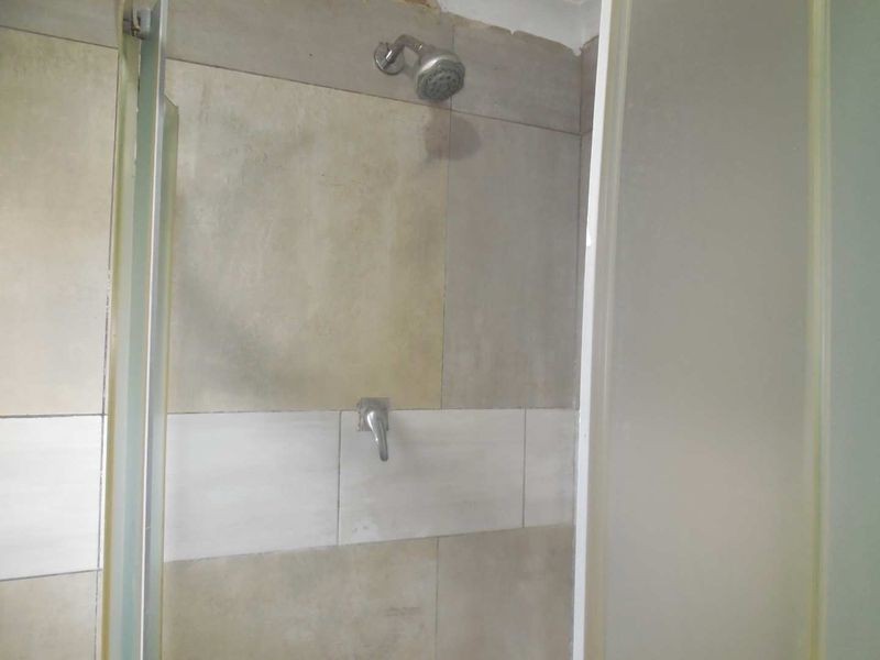 A functional shower enclosure featuring tiled walls, a standard shower head, and a glass door, currently showing signs of wear.