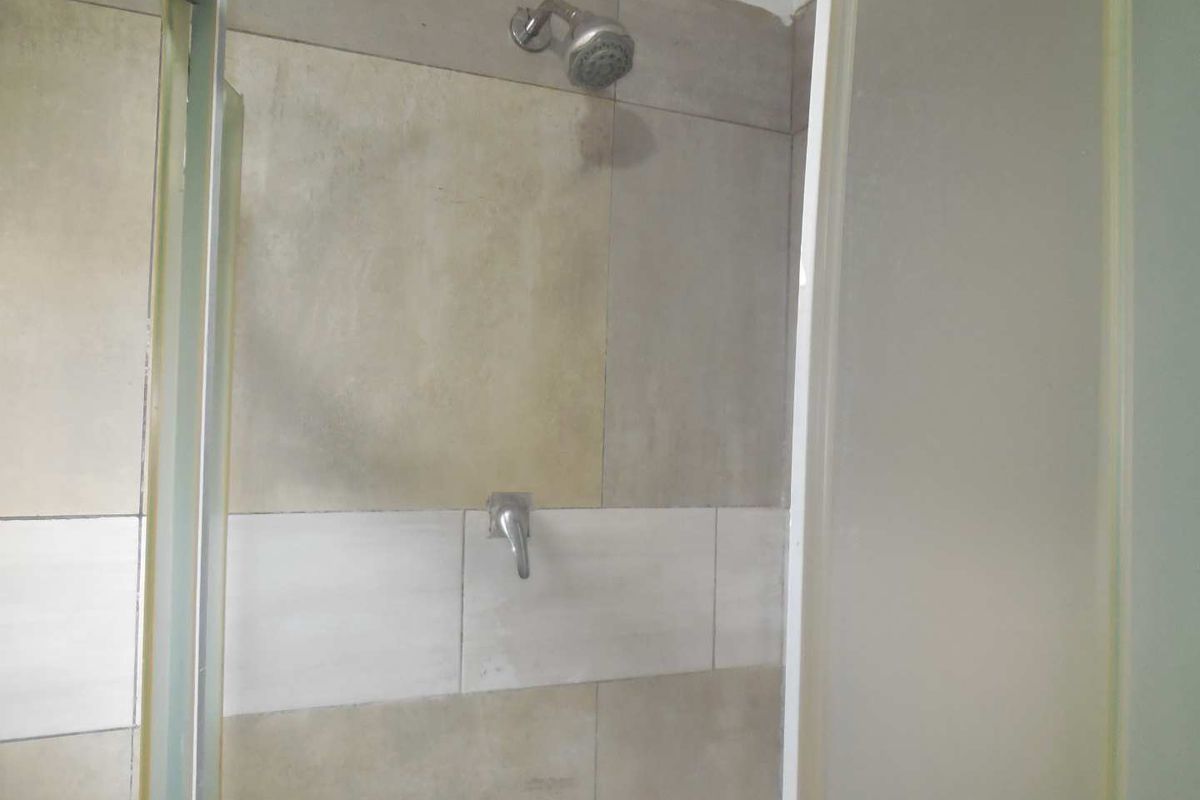 A functional shower enclosure featuring tiled walls, a standard shower head, and a glass door, currently showing signs of wear.