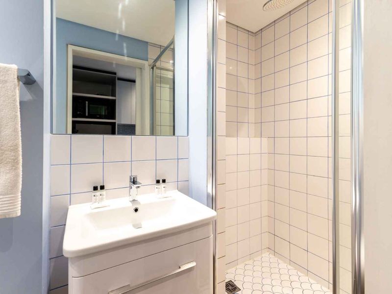 A clean, modern bathroom featuring a white vanity cabinet, basin, mirror, and a tiled shower enclosure with a rainfall shower head.