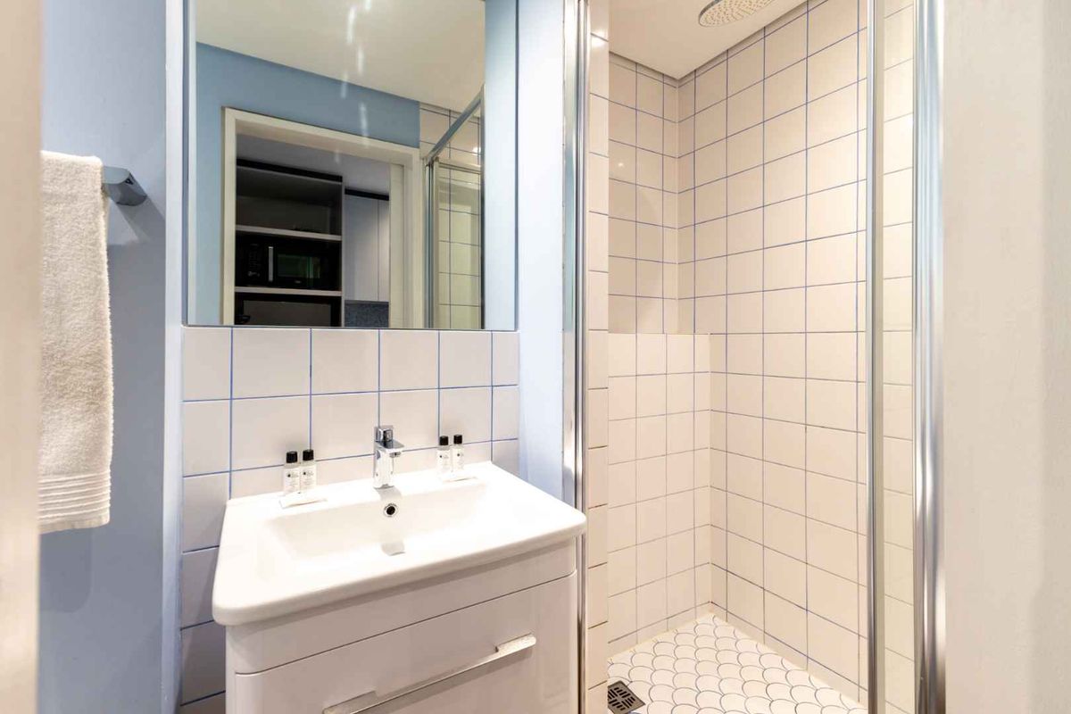 A clean, modern bathroom featuring a white vanity cabinet, basin, mirror, and a tiled shower enclosure with a rainfall shower head.