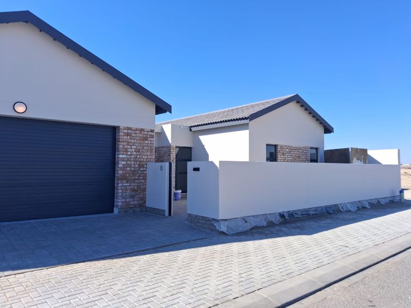 Front elevation of a modern house featuring a brick and plaster facade, automated garage, and paved driveway with a perimeter boundary wall.