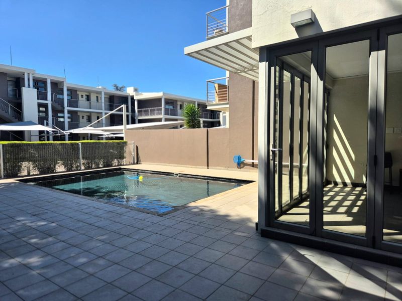 Private swimming pool area with tiled patio and modern folding glass doors leading into the apartment.