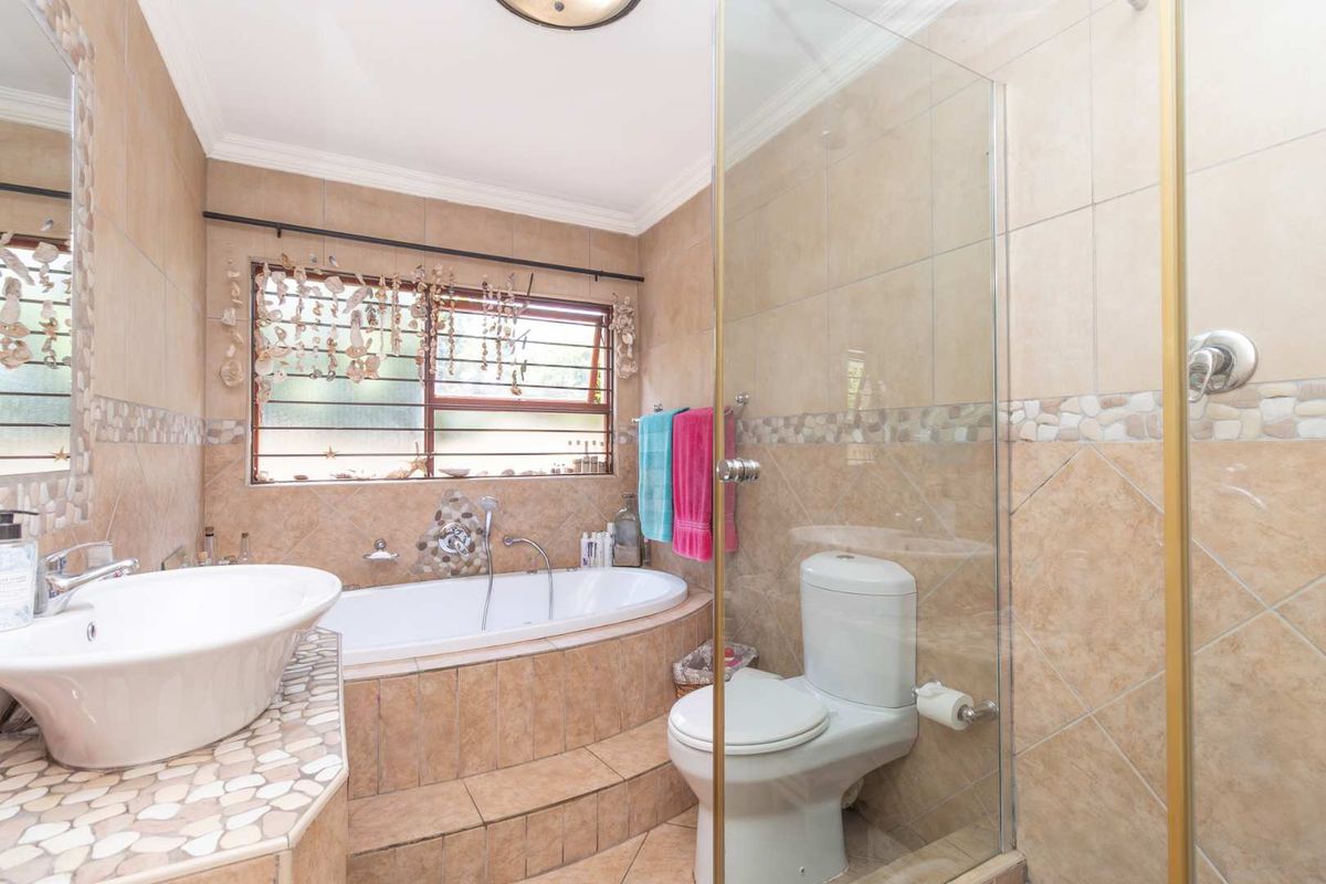A functional bathroom featuring a built-in bathtub, a separate glass-enclosed shower, a vanity basin, and tiled walls with decorative mosaic accents.