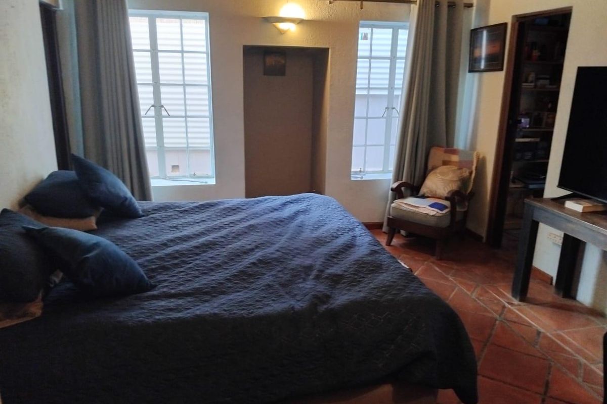 A bedroom featuring terracotta floor tiles, dual windows with curtain rods, and a central wall niche, providing a cozy and functional living space.