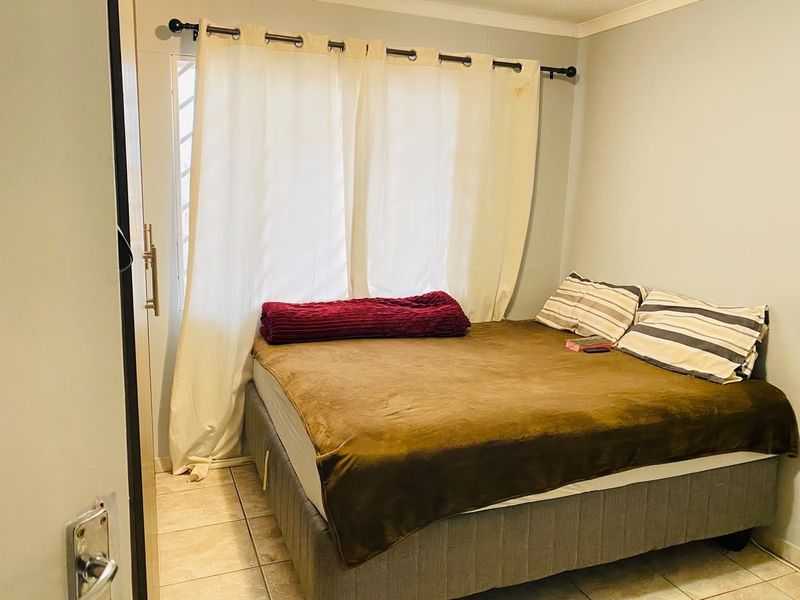 A compact bedroom featuring tiled flooring and a window with curtain fixtures.