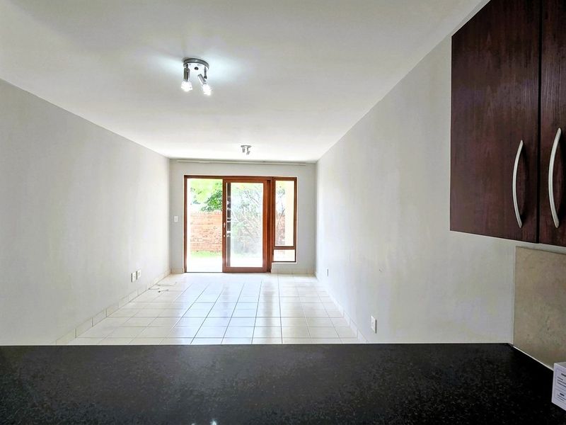 An open-plan living area featuring tiled flooring, neutral walls, and a sliding glass door leading to the exterior, viewed from the kitchen counter.