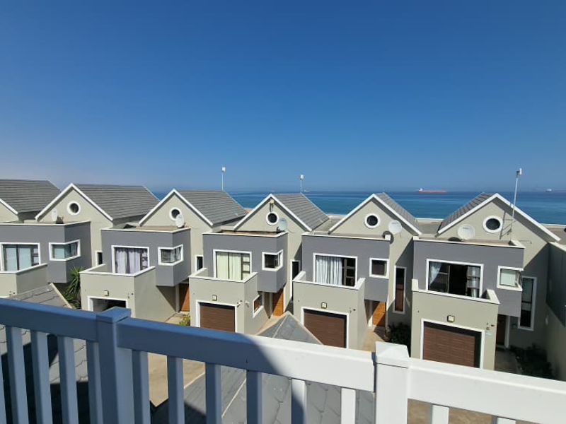 Elevated view overlooking a row of modern townhouse units with tiled roofs and garages, featuring a clear ocean horizon in the background.