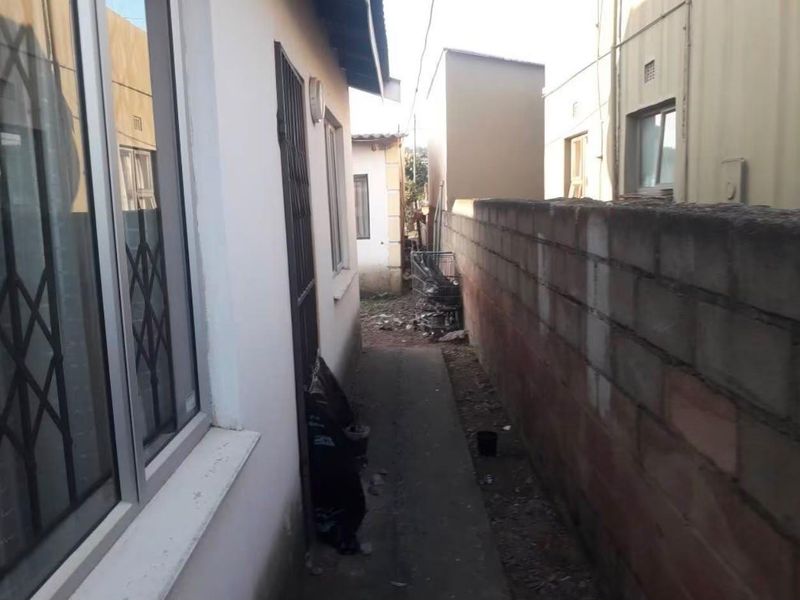 A narrow side passage between the house and a concrete boundary wall, featuring aluminium window frames and a security gate.