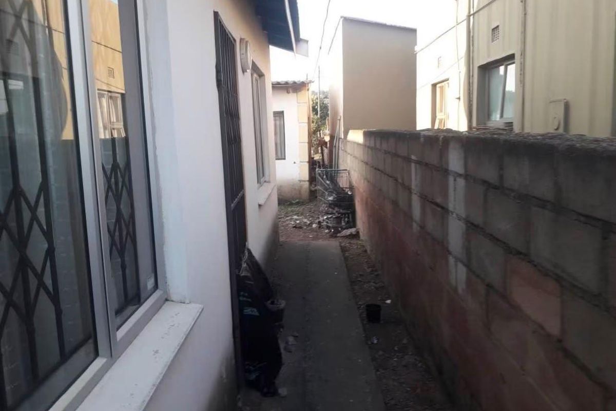 A narrow side passage between the house and a concrete boundary wall, featuring aluminium window frames and a security gate.