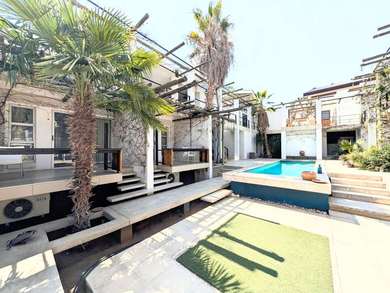 Outdoor pool area featuring a raised swimming pool, timber pergola structures, and concrete decking, providing a communal entertainment space for the guest house.