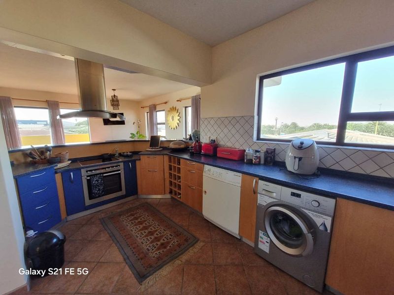Functional kitchen featuring laminate cabinetry, built-in oven with extractor fan, tiled backsplash, and terracotta flooring with integrated laundry appliance space.