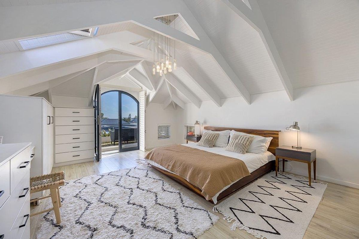 Spacious bedroom featuring a high vaulted ceiling with exposed rafters, skylights, and an arched glass door leading to an outdoor area.