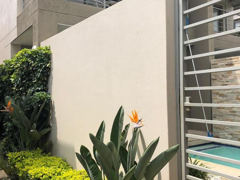 A well-maintained rear exterior area featuring a private swimming pool, stone-clad feature wall, metal security gate, and a balcony above.