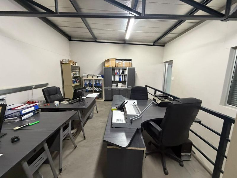Functional office space featuring exposed steel roof trusses, concrete flooring, and a mezzanine-style layout with a metal safety balustrade.