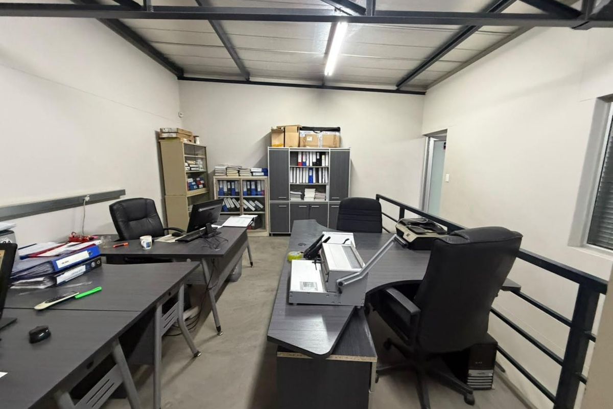 Functional office space featuring exposed steel roof trusses, concrete flooring, and a mezzanine-style layout with a metal safety balustrade.