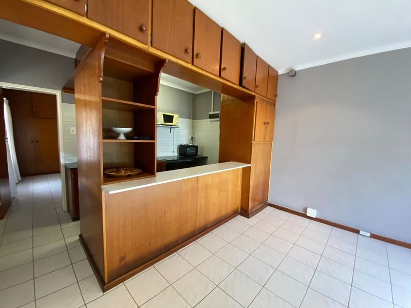 Open plan kitchen and living area featuring extensive built-in wooden cabinetry, a breakfast bar, and neutral tiled flooring throughout.