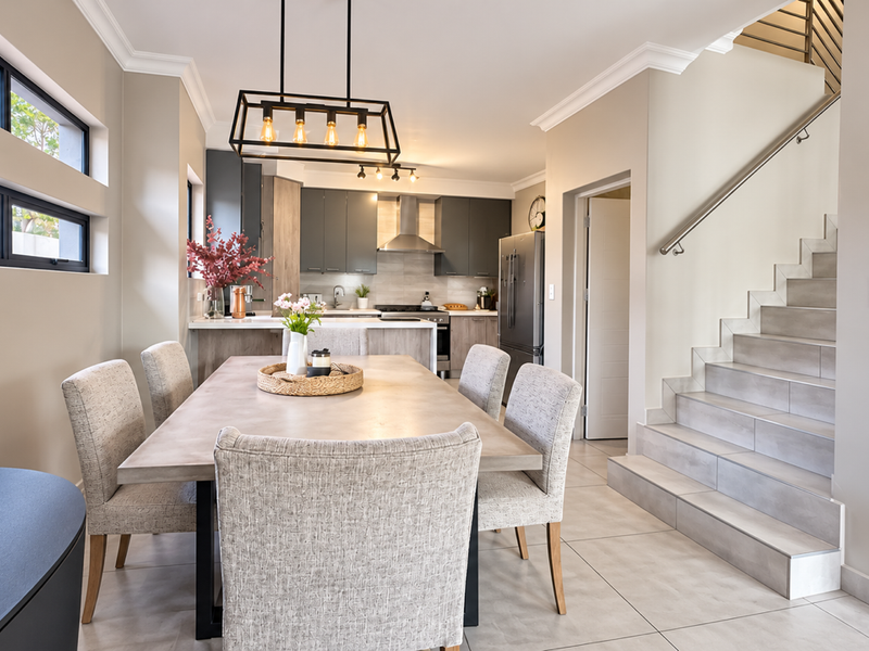 Modern open-plan living area featuring a sleek kitchen with built-in appliances, tiled flooring, and a contemporary staircase with a stainless steel handrail.