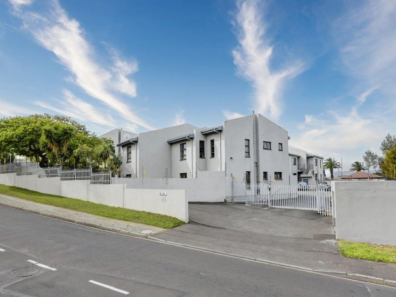 Front exterior view of the apartment complex featuring a secure gated entrance, asphalt driveway, and perimeter wall with electric fencing.