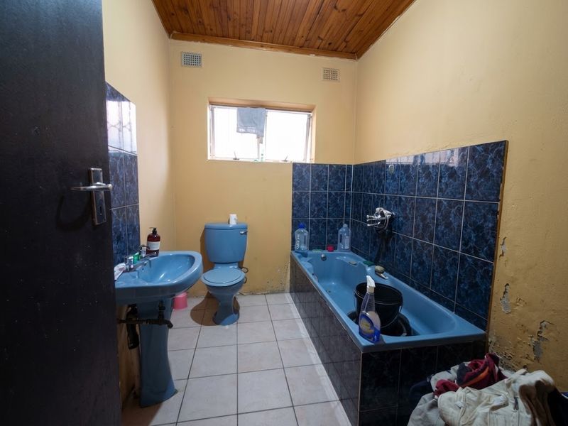 A dated bathroom featuring blue sanitaryware, tiled splashbacks, and a timber ceiling, currently requiring cosmetic updates and wall repairs.