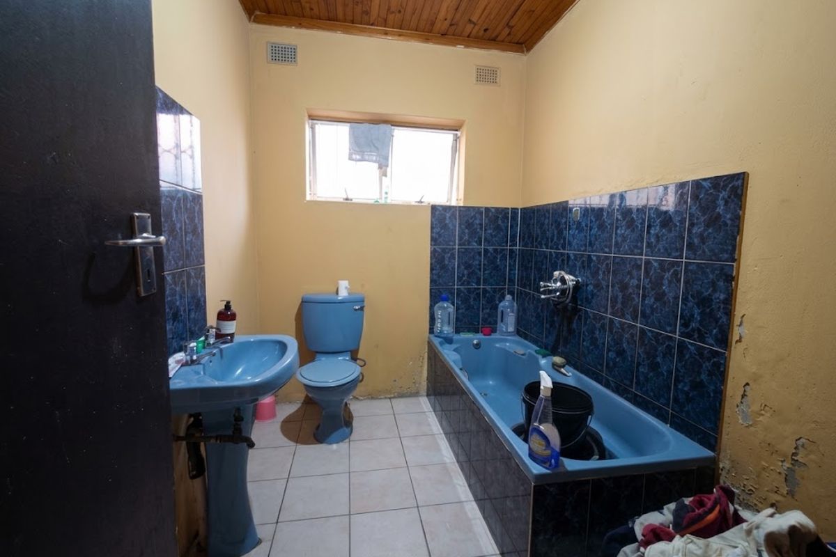 A dated bathroom featuring blue sanitaryware, tiled splashbacks, and a timber ceiling, currently requiring cosmetic updates and wall repairs.