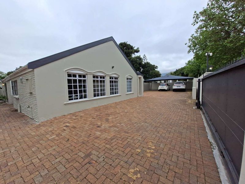 A well-maintained front exterior featuring a brick-paved driveway, secure sliding gate, and a covered carport area alongside the main building structure.
