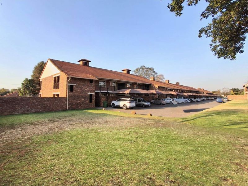 Exterior view of a multi-unit apartment complex featuring face-brick construction, tiled roofing, and dedicated covered parking bays within a landscaped residential estate.