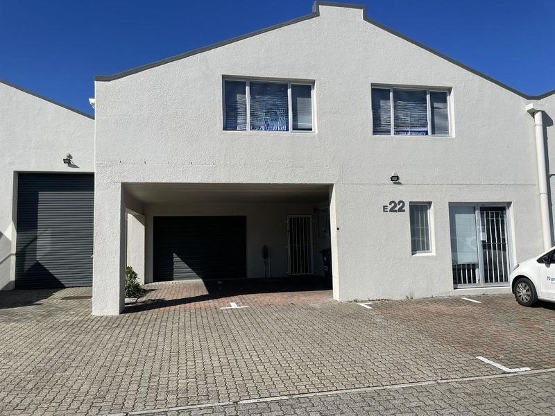 Front elevation of a commercial unit featuring a paved driveway, roller shutter garage door, and secure entrance access.
