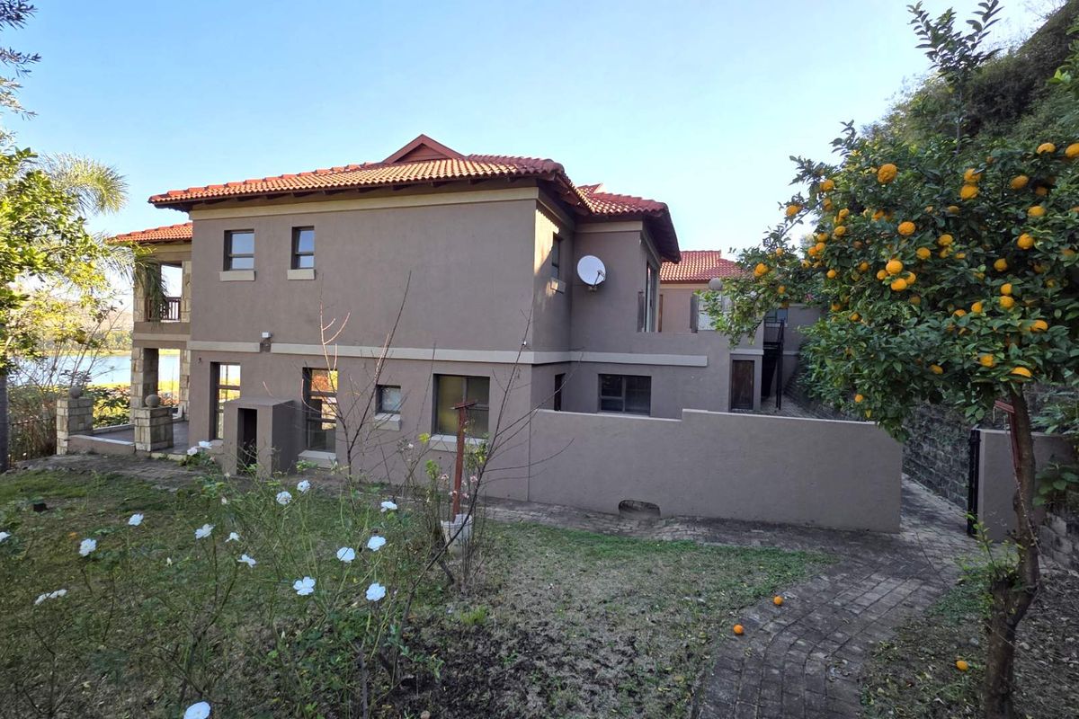 Rear view of a multi-story residential property featuring a tiled roof, neutral exterior walls, and a landscaped garden with a paved walkway.