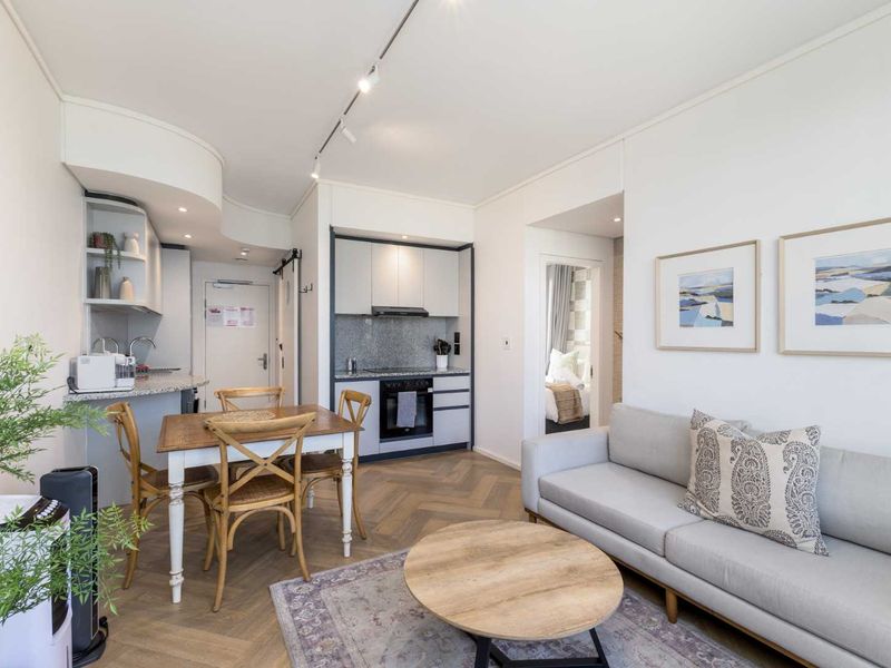 Modern open-plan living area featuring a compact kitchen with built-in cabinetry, granite countertops, integrated oven, and stylish herringbone flooring.