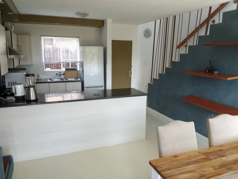Open plan kitchen and dining area featuring a breakfast bar, modern cabinetry, and a staircase with integrated shelving.