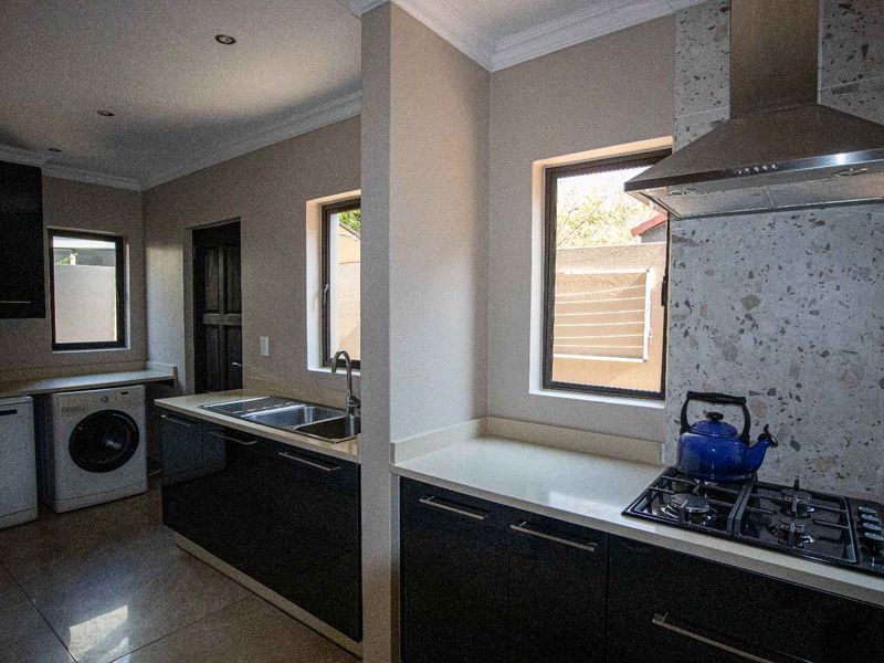 Modern kitchen featuring dark cabinetry, stone countertops, gas hob with extractor fan, and integrated laundry area with tiled flooring.