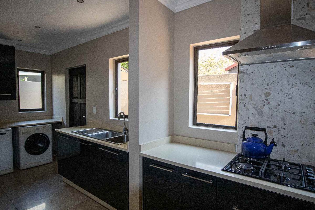 Modern kitchen featuring dark cabinetry, stone countertops, gas hob with extractor fan, and integrated laundry area with tiled flooring.