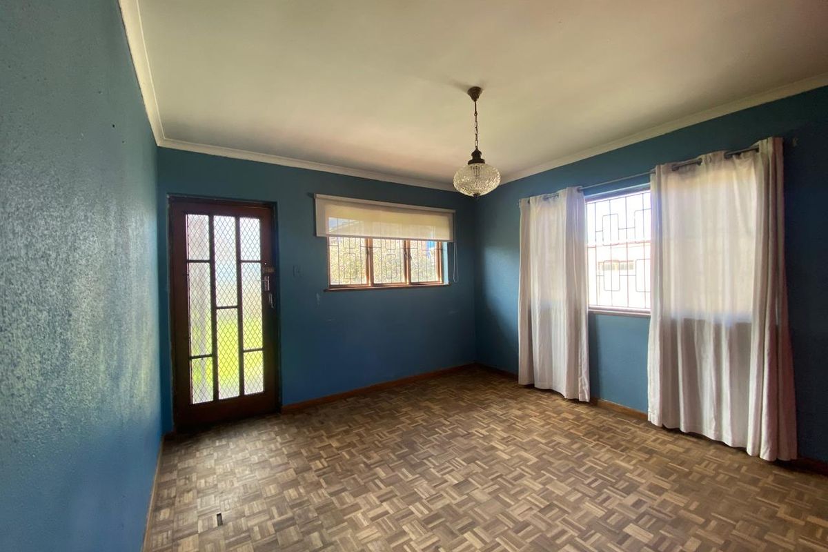 A vacant living room featuring original parquet flooring, blue painted walls, and security bars on the windows and exterior door.
