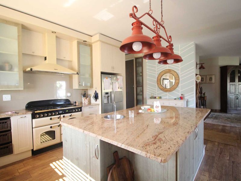A well-appointed kitchen featuring a large granite-topped island, built-in oven with gas hob, extractor fan, and custom cabinetry, finished with warm hardwood flooring.