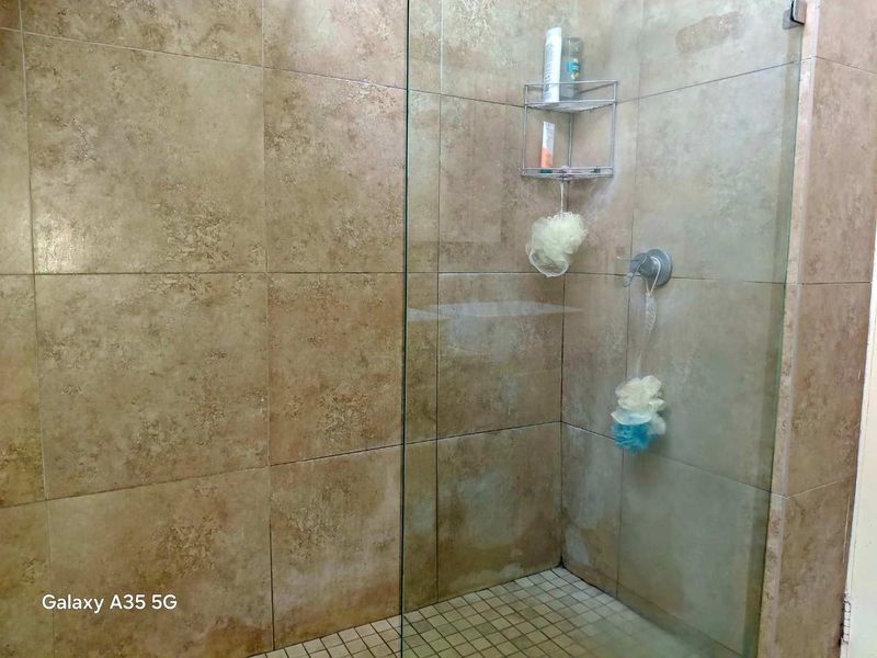 A shower enclosure featuring beige wall tiles, a mosaic tiled floor, and a glass screen with a built-in mixer tap.