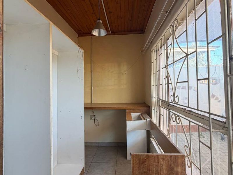 A functional scullery or utility area featuring tiled floors, a wooden ceiling, and built-in cabinetry, requiring some cosmetic updates and finishing touches.