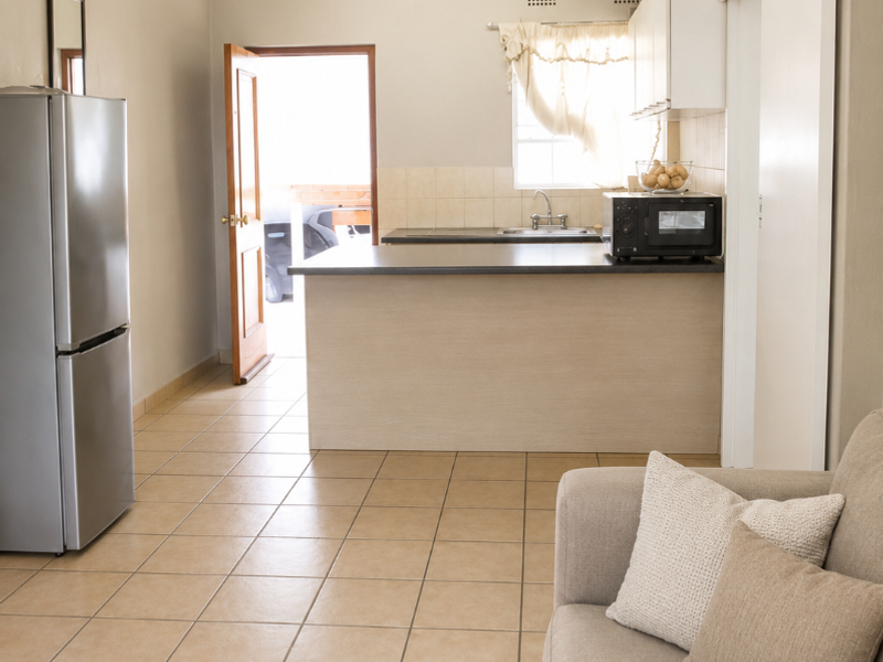 An open-plan living and kitchen area featuring tiled flooring, neutral wall tones, and a functional kitchen layout with built-in cabinetry and countertop space.