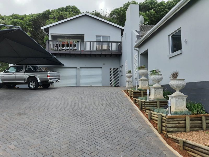 Front exterior view of the property featuring a paved driveway, double garage, and an elevated balcony with a landscaped garden border.