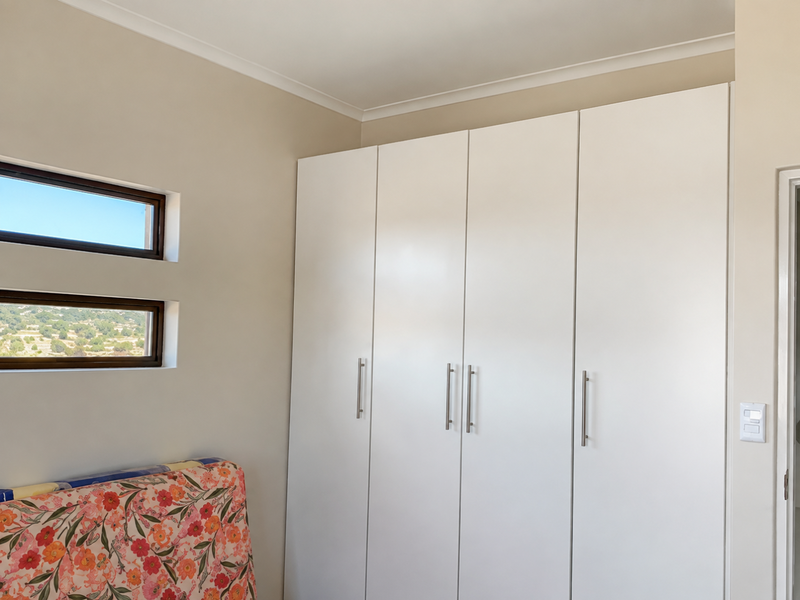 A bedroom featuring modern white built-in cupboards and dual horizontal windows providing natural light and scenic views.