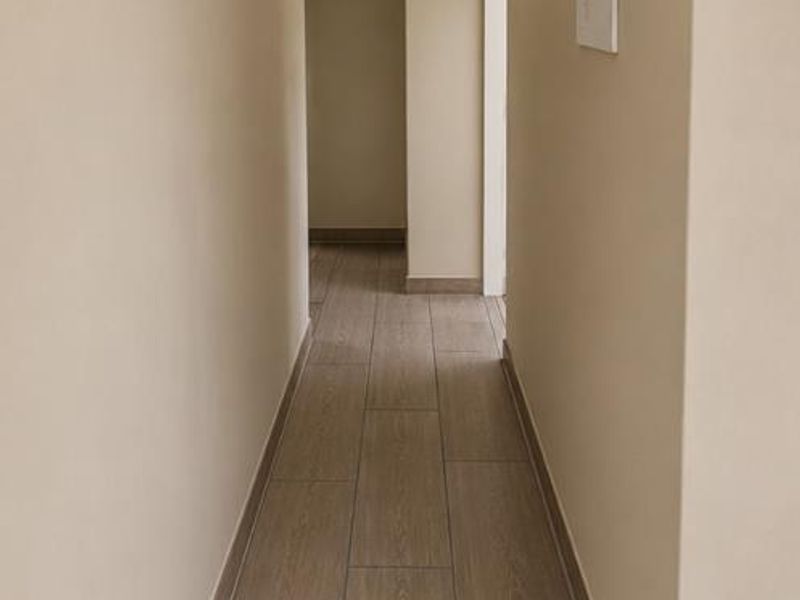 A clean, well-maintained hallway featuring neutral walls, modern flush mount lighting, and wood-look tiled flooring.