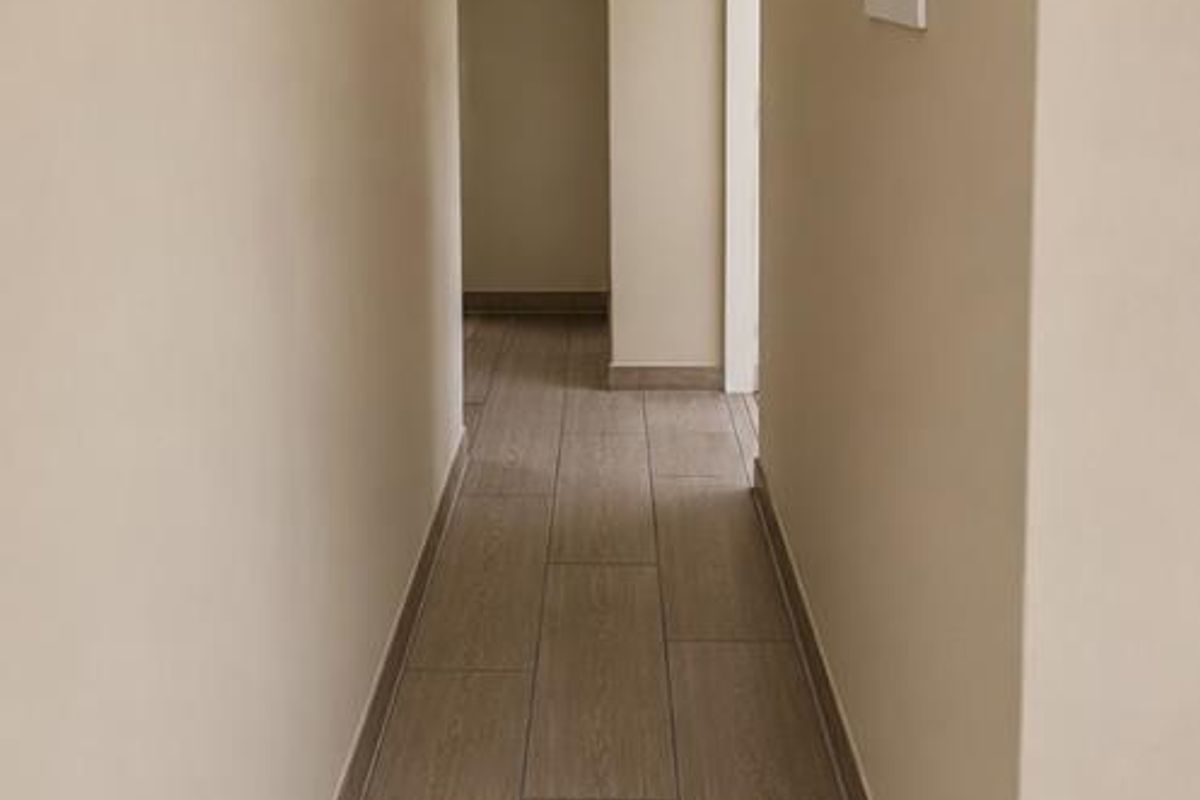 A clean, well-maintained hallway featuring neutral walls, modern flush mount lighting, and wood-look tiled flooring.