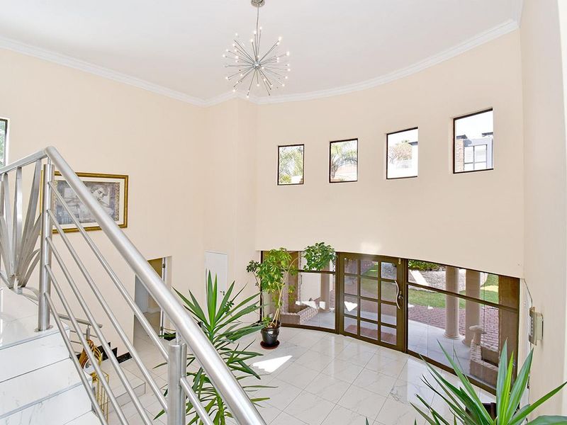 Spacious double-volume entrance hall featuring tiled flooring, a modern stainless steel staircase railing, and abundant natural light through large glass doors and clerestory windows.