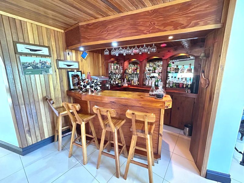 A dedicated home bar area featuring extensive wood paneling, a built-in wooden bar counter, and a mirrored back bar with integrated glassware storage.