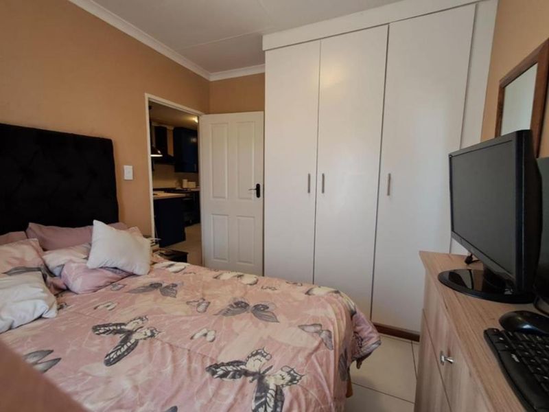 A functional bedroom featuring built-in wardrobes, tiled flooring, and coved ceiling details, with a view into the adjacent kitchen area.