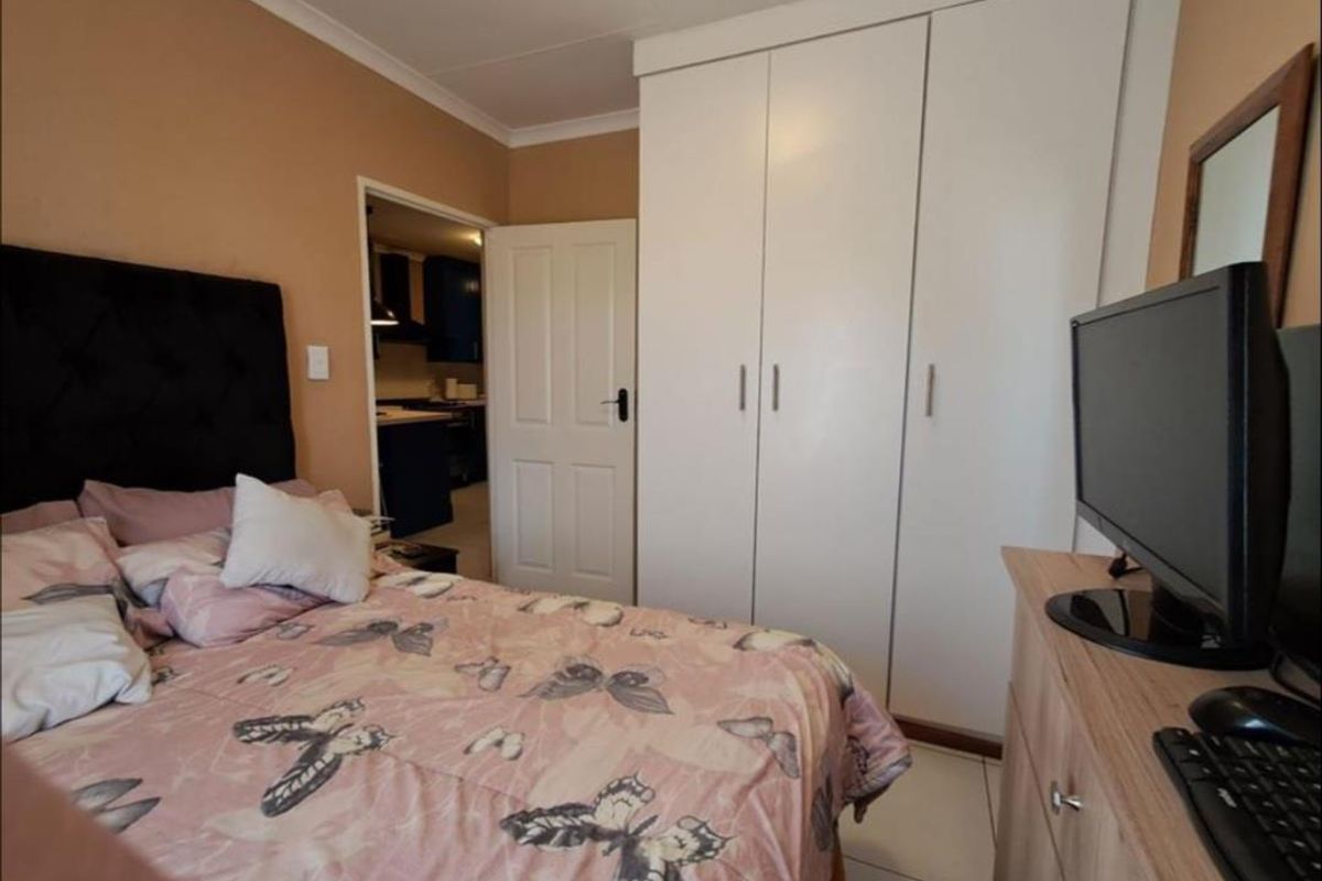 A functional bedroom featuring built-in wardrobes, tiled flooring, and coved ceiling details, with a view into the adjacent kitchen area.