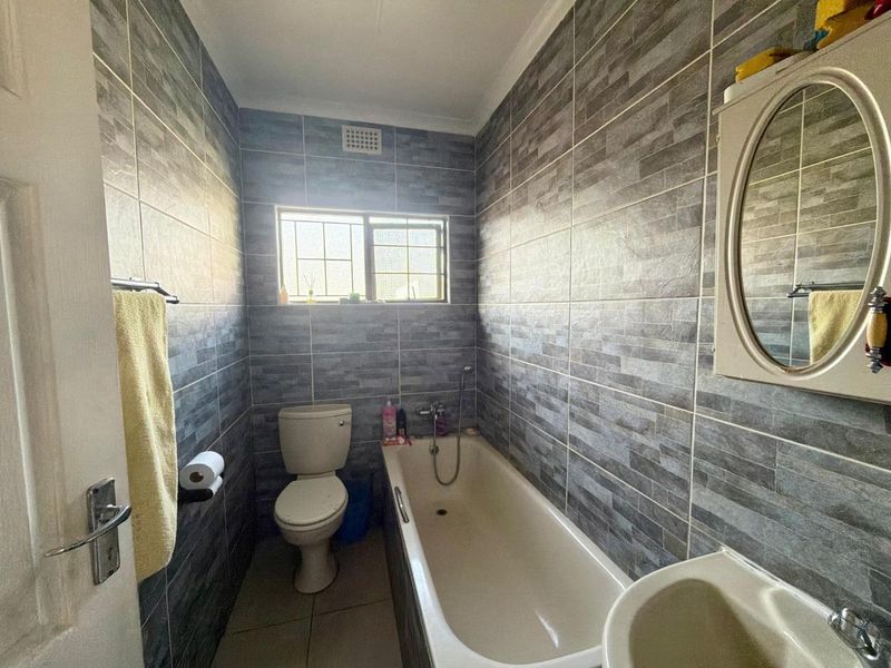 A compact bathroom featuring full-height grey textured wall tiles, a standard bathtub, toilet, and basin with a wall-mounted mirror cabinet.
