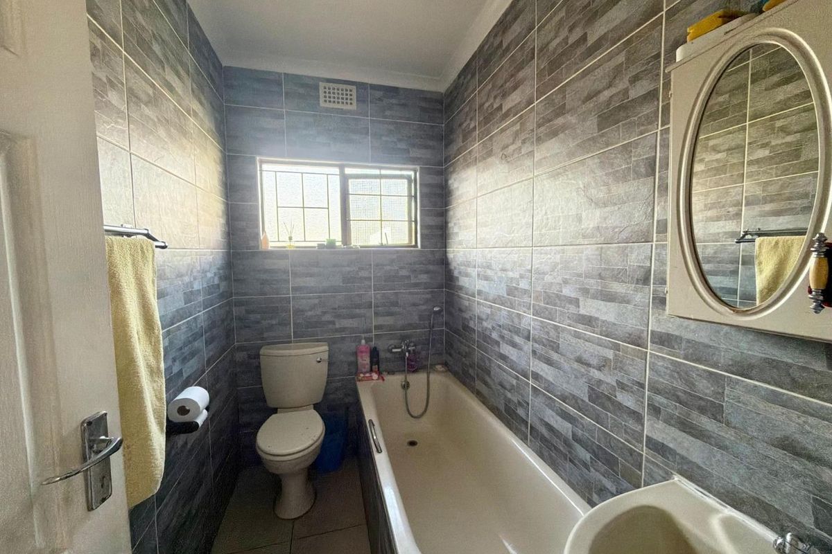 A compact bathroom featuring full-height grey textured wall tiles, a standard bathtub, toilet, and basin with a wall-mounted mirror cabinet.