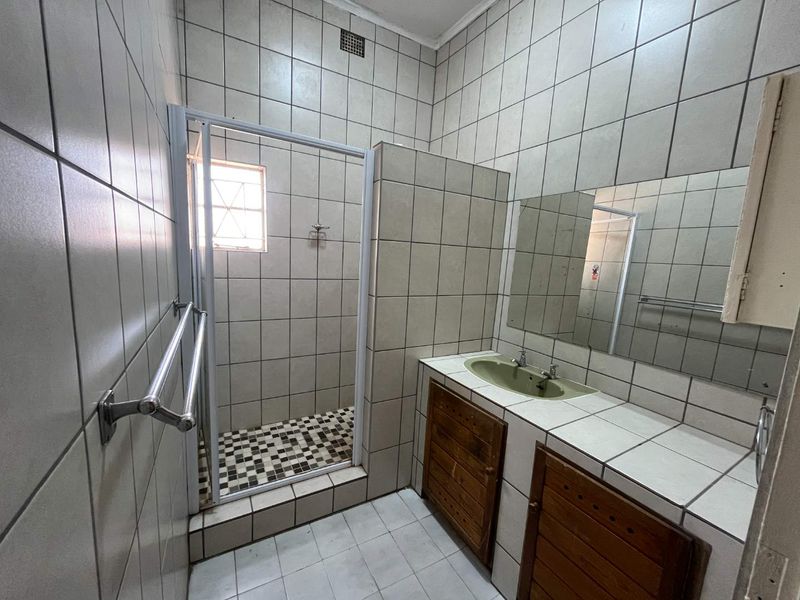 A functional bathroom featuring a tiled shower enclosure, built-in vanity with storage, and wall-mounted mirror, presenting an opportunity for modern cosmetic updates.
